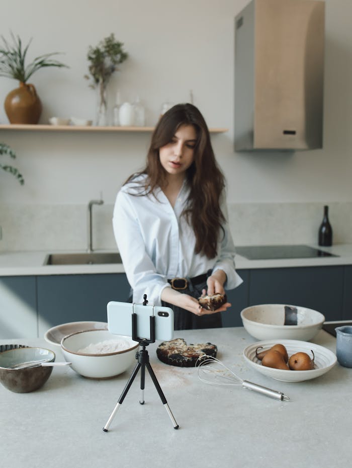 services-07 Woman creating a cooking blog video in a modern kitchen with phone on tripod.